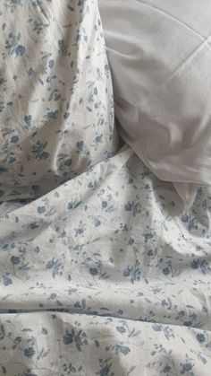 an unmade bed with white sheets and blue flowers