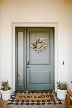 a door with a wreath on it and two potted plants in front of it