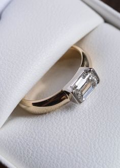 an engagement ring with a baguette cut diamond sits in a white velvet box