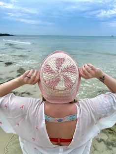 a woman standing on top of a beach next to the ocean holding her hat over her head