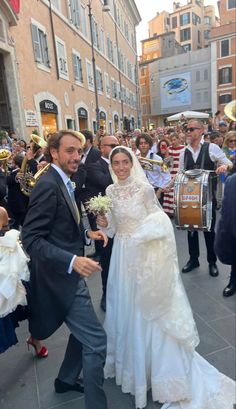 a bride and groom walking down the street in front of a large group of people