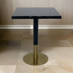 a black table with a gold base on the floor in front of a beige wall