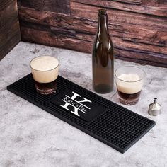 two beer glasses sitting on top of a mat next to a bottle