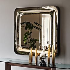 a mirror sitting on top of a table next to a vase with a plant in it