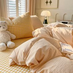 a teddy bear sitting on top of a bed next to pillows and blankets with the sheets pulled down