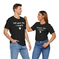 This 'Tell Your Dog I Said Hi Paw Print' Unisex Jersey Short Sleeve Tee gives off a fun and friendly vibe, perfect for dog lovers who just love all dogs. It can be worn casually or dressed up, making it versatile for everyday wear. Ideal for dog owners, animal lovers, and pet enthusiasts. Relevant for dog-themed holidays, pet birthdays, and casual outings. Product features - Made with 100% Airlume combed and ring-spun cotton, lightweight and breathable - Retail fit perfect for casual and semi-fo Black Crew Neck T-shirt With Dog Print, Black Cotton Dog Print Top, Black Cotton Top With Dog Print, Black Graphic Tee With Dog Print, Dog Print Crew Neck Graphic Tee, Relaxed Fit Short Sleeve Tops With Dog Print, Cotton Crew Neck Top With Dog Print, Funny Dog Print Crew Neck T-shirt, Dogs Paw Print