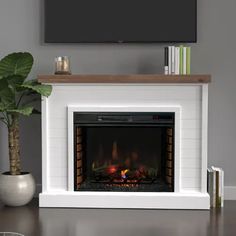 a white fireplace with a flat screen tv above it and a potted plant on the table