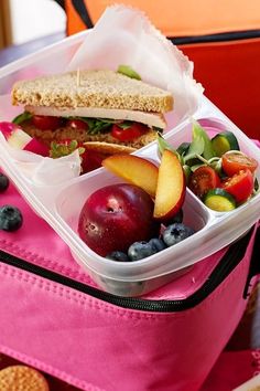 a lunch box filled with fruit and sandwich on top of a pink baggy sack