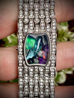 Gemstone-filled shaker locket up-cycled designer wrist watch, silver tone with pave rhinestone, opal, amethyst, aquamarine, topaz, unique gift for her. A kaleidoscope on your wrist! Formerly a blingy wrist watch, inlaid with pave rhinestones on the top of the wrist. Now, minus the mechanism, I've filled the space with a collection of colourful gems. Most notable is a large chunk of raw Ethiopian opal in a gorgeous deep iridescent green. A constantly shifting mix of blue, purple, green, and a few Upcycled Jewelry Diamond, Iridescent Green, Unique Gifts For Her, Purple Green, Chain Link Bracelet, Ethiopian Opal, Link Bracelets, Blue Purple, Chain Link