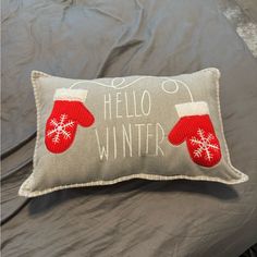 a gray pillow with red mittens and the words hello winter written in white on it