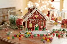 a gingerbread house on a table surrounded by candies and candy canes in glass jars