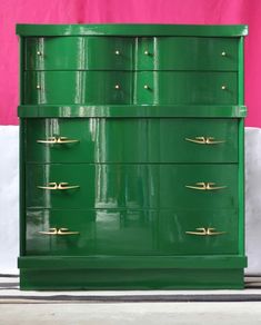 a green dresser with gold handles in front of a pink wall and white flooring