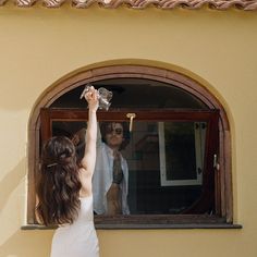 a woman reaching up to grab something out of the window with her hand while another woman looks on