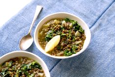 two bowls filled with lentils and greens on top of a blue towel next to a spoon