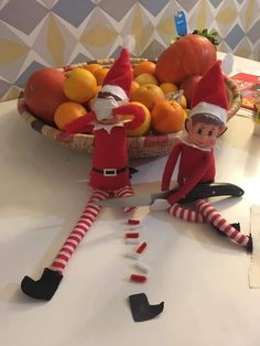 two elfs sitting in front of a bowl of fruit on a table with scissors