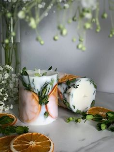 an orange slice is next to a candle and some flowers on a white counter top