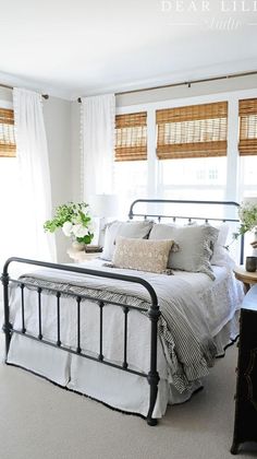 a bedroom with white bedding and black iron bedspread, window curtains, and flowers in vases