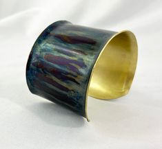 These unique, hand-formed copper and brass cuff bracelets with vibrant patinas create stunning accents to your personal style. Dress up or down- either way you'll be wearing an adornment that will turn heads, start conversations, and delight the eye of the beholder. This is a wide, flanged Brass cuff with a beautiful blue and purple heat patina. Please note that patina colors may look different depending on the screen/device you view them on. This is a medium cuff, see measurements below. Cuffs Adjustable Blue Patina Cuff Bracelet, Adjustable Blue Cuff Bracelet With Patina, Blue Patina Cuff Bracelet As A Gift, Blue Patina Cuff Bracelet As Gift, Blue Cuff Bracelet With Patina As A Gift, Blue Cuff Bracelet With Patina For Gifts, Brass Cuff Bracelet With Patina As A Gift, Artistic Adjustable Patina Cuff Bracelet, Adjustable Patina Cuff Bracelet