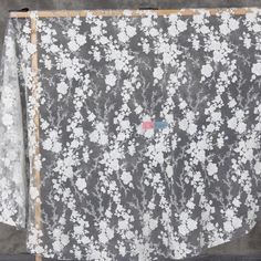 an image of a white and grey floral pattern on sheer fabric hanging from a wooden frame