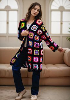 a woman standing in front of a couch wearing a colorful crochet jacket and jeans