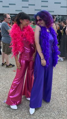 two women dressed in purple and pink standing next to each other at a festival or gathering