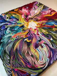 a colorful piece of art made out of yarn and thread on top of a table