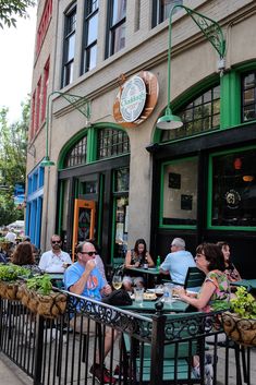 people sitting at tables in front of a restaurant with green doors and windows on the side walk