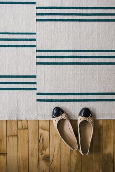 two pairs of shoes sitting on top of a wooden floor next to a striped rug