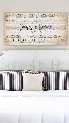 a white bed topped with pillows under a wooden sign above it's headboard