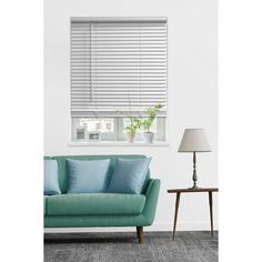 a living room with a green couch and white blinds on the window sill, next to a lamp