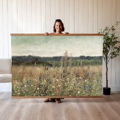 a woman holding up a large painting in front of her face