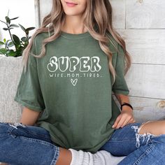 a woman sitting on the floor with her legs crossed wearing ripped jeans and a t - shirt that says, super wife