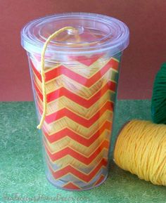 a cup with yarn next to it and a ball of yarn on the ground behind it