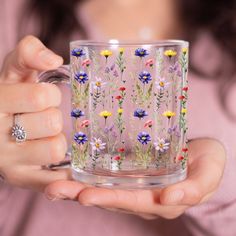 a woman holding a glass mug with flowers painted on it