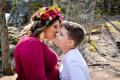 a woman kissing a boy on the cheek in front of some trees and rocks,