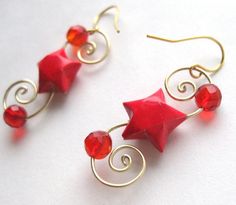 red earrings with gold spirals and star shaped beads on them, sitting on a white surface