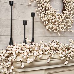 a wreath is hanging on the wall above a mantle with white flowers and black candles