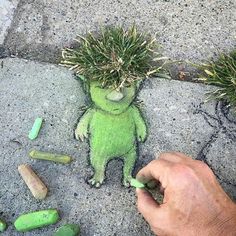 a person is drawing on the sidewalk with crayons and grass in front of them