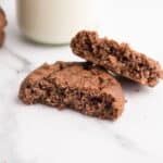 two chocolate cookies next to a glass of milk