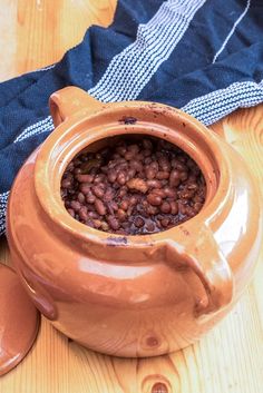 a brown pot filled with beans sitting on top of a wooden table