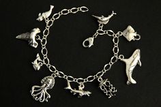 A collection of silver plated marine life themed charms have been dispersed around a shimmering silver plated bracelet chain in this handmade charm bracelet. This sea predator charm bracelet is then completed with a lobster clasp and a 1/2 inch of chain at the end for adjustable sizing. Charms in this bracelet include a seal charm, shark tooth charm, whale charm, octopus charm, shark charm, jellyfish charm, orca charm, stingray charm, and swordfish charm. ● Sizing ● To determine your bracelet si Ocean-inspired Silver Bracelets As Gifts, Ocean-inspired Charm Bracelet As A Gift, Ocean-inspired Silver Charms Jewelry, Ocean-inspired Charm Bracelet Gift, Themed Sterling Silver Charms, Themed Silver Sterling Charms, Handmade Silver Ocean-inspired Bracelets, Handmade Ocean-inspired Charm Bracelet As A Gift, Handmade Ocean-inspired Charm Bracelet For Gifts