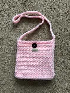 a pink crocheted purse laying on the ground with a black button in it