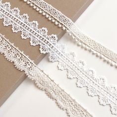 three white lace trims sitting on top of a piece of brown paper next to each other