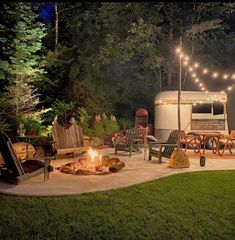 a camper trailer is lit up at night with string lights and chairs around the fire pit