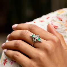 The Story A beautiful Art Deco dinner ring from the 1920s. At center is a half carat old mine cut diamond. Two square cut emeralds are bezel set above and below, each measuring 5 x 4.5 mm. Accenting the piece are eight old mine cut diamonds, each 0.07- 0.08 carats, giving the ring a total diamond weight of approximately 1.12 carats. The back is completely open allowing the diamonds to sparkle bright and the emeralds to pop with color. Measuring just under an inch tall, the shape and size has a substantial feel. The 18k white gold design allows for open work and millegrain detailing throughout. Worn as an engagement ring or a cocktail ring, this beautiful piece is sure to stop you in your tracks. The Specs Style Number: R2533 Antique, circa 1920s 18 karat white gold 2 square cut emeralds, e Heirloom Emerald-cut Ring With Single Cut Diamonds, Heirloom Emerald Cut Ring With Single Cut Diamonds, Art Deco Emerald Cut Emerald Ring For Promise, Art Deco Emerald Cut Emerald Promise Ring, Art Deco Emerald Cut Diamond Jewelry, Art Deco Emerald Cut Emerald Jewelry, Art Deco Emerald Cut Jewelry, Art Deco Emerald Diamond Ring For Wedding, Art Deco Green Emerald Ring With Rose Cut Diamonds