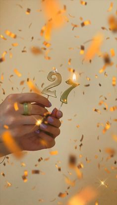 a person holding a lit candle in front of confetti falling from the sky