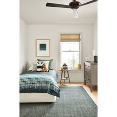 a bed room with a neatly made bed and a ceiling fan in the corner next to a window