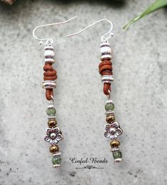 a pair of silver and leather earrings with flowers on them sitting on a concrete surface