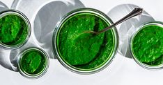 four jars filled with green pestle on top of a white tablecloth next to spoons