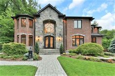 a large brick house with lots of windows on the front and side of it, surrounded by lush green trees